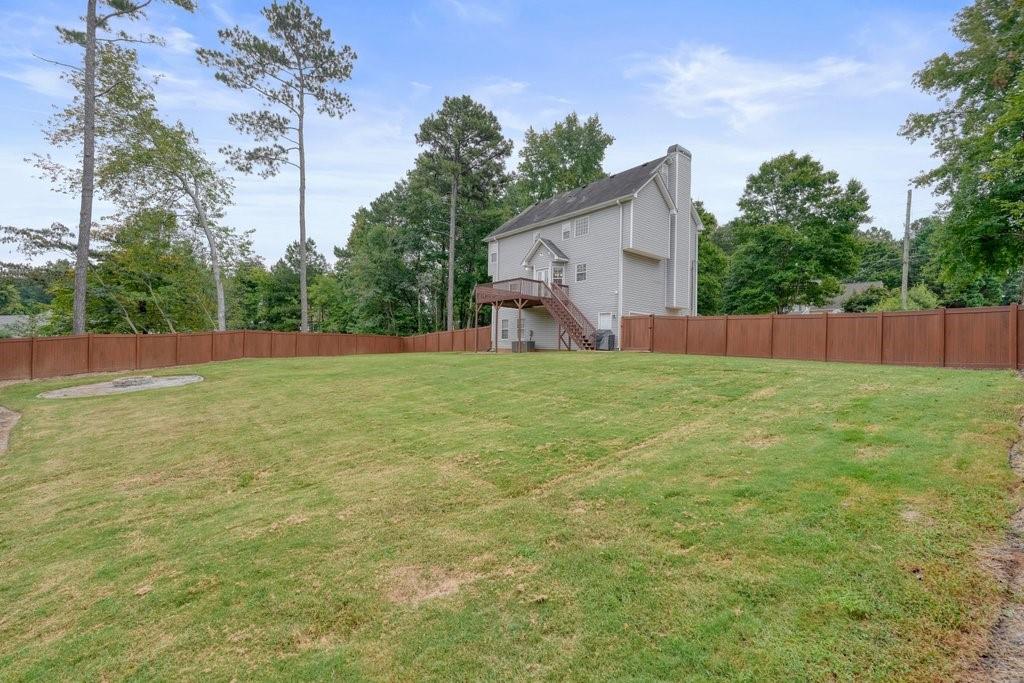 Grassy backyard enclosed by a privacy fence, with a two-story gray house and raised deck.