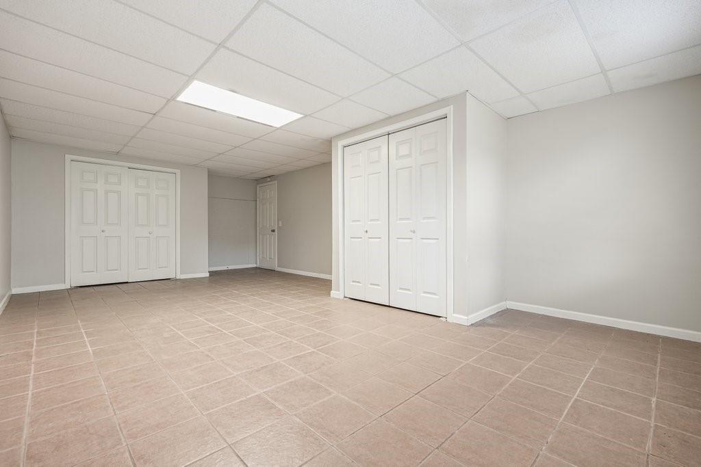 Empty tiled room with several white closet doors and a suspended ceiling.