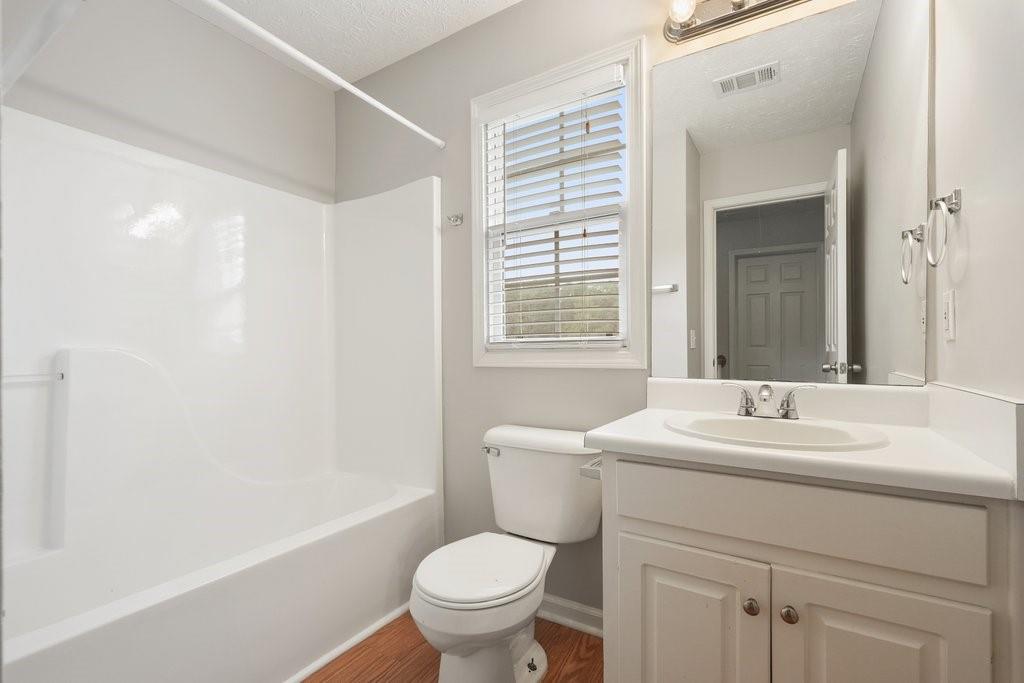 Bathroom with a white tub and shower, toilet, and vanity beneath a window with blinds.