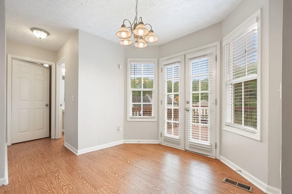 Empty dining area with wood-look flooring, chandelier, and glass doors opening to a deck.