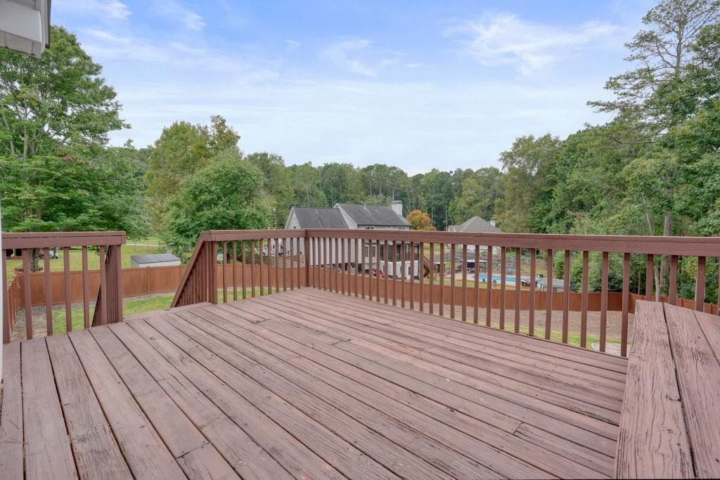 Backyard deck overlooking a fenced yard, neighboring pool, and wooded tree line.