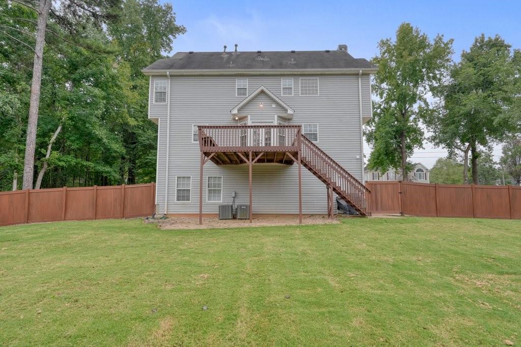 Rear of a two-story gray house with a raised deck and stairs overlooking a fenced lawn.