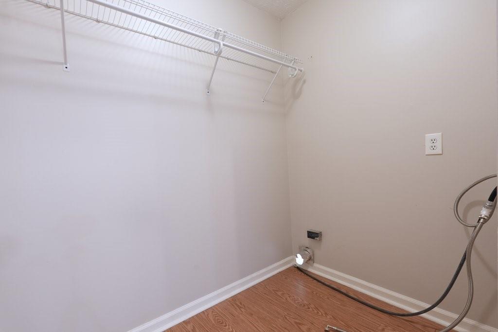 Empty laundry room with wire shelving, washer and dryer hookups, and wood-look flooring.