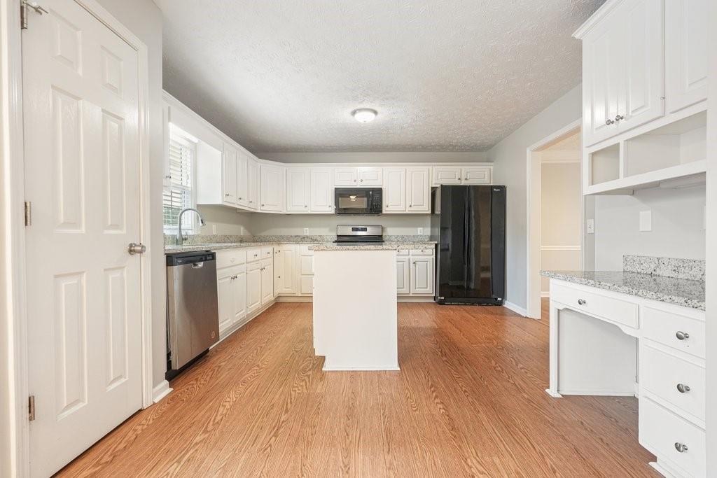 Kitchen with white cabinetry, granite counters, black appliances, and a central island.