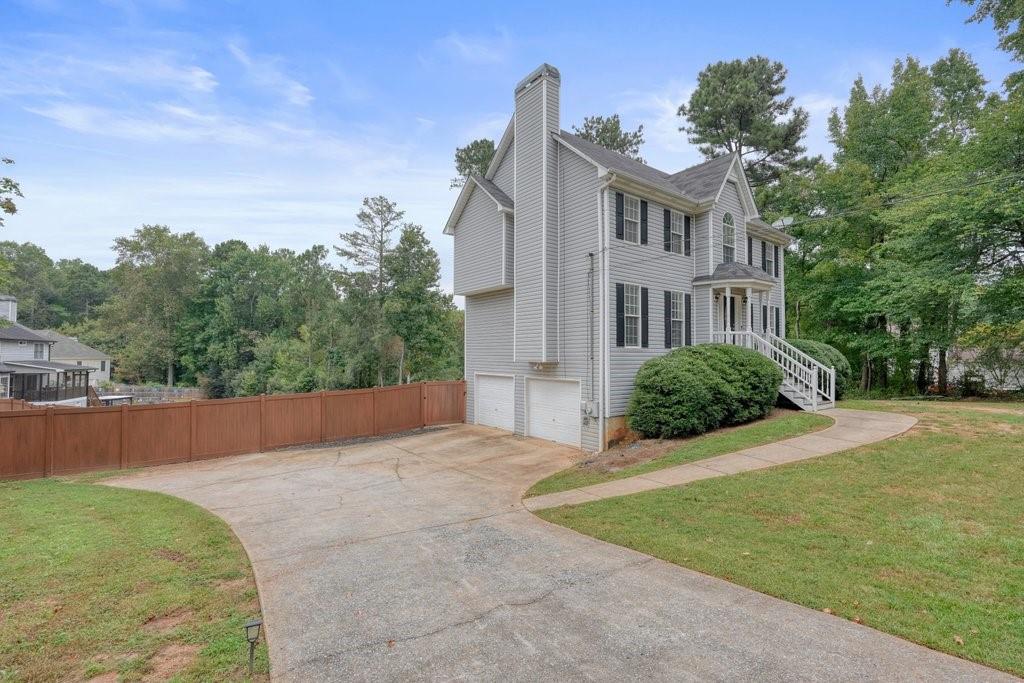 Gray two-story house with white trim, double garage, curved driveway, and fenced yard.