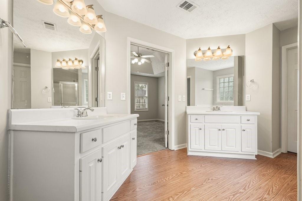 Bathroom with two white vanities, large mirrors, and warm wood flooring.