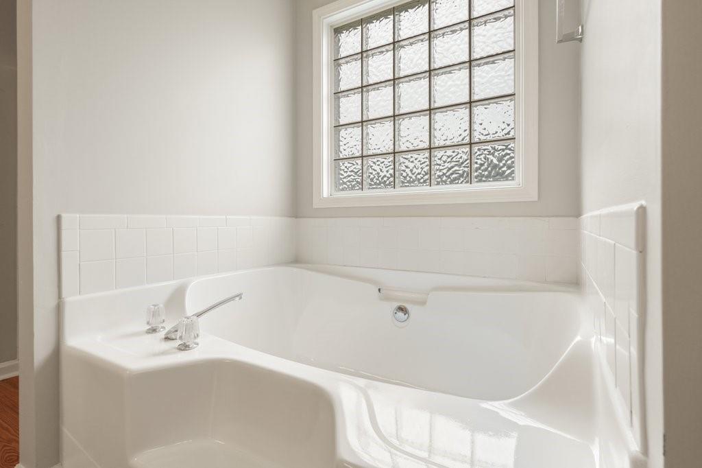 Bright bathroom with a built-in white bathtub beneath a textured-glass window.