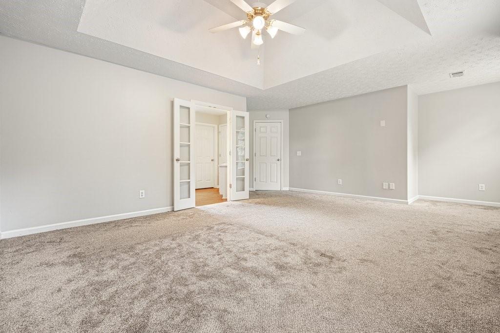 Empty carpeted room with a vaulted ceiling, ceiling fan, and open French doors.