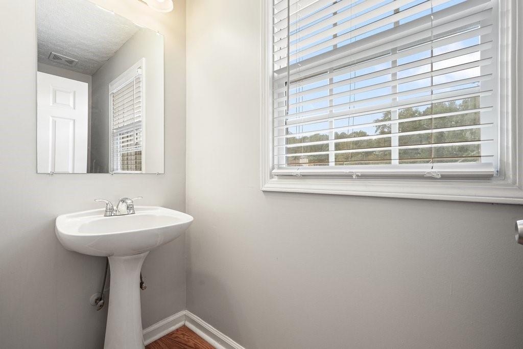 Bathroom with a white pedestal sink, wall mirror, and large window with white blinds.