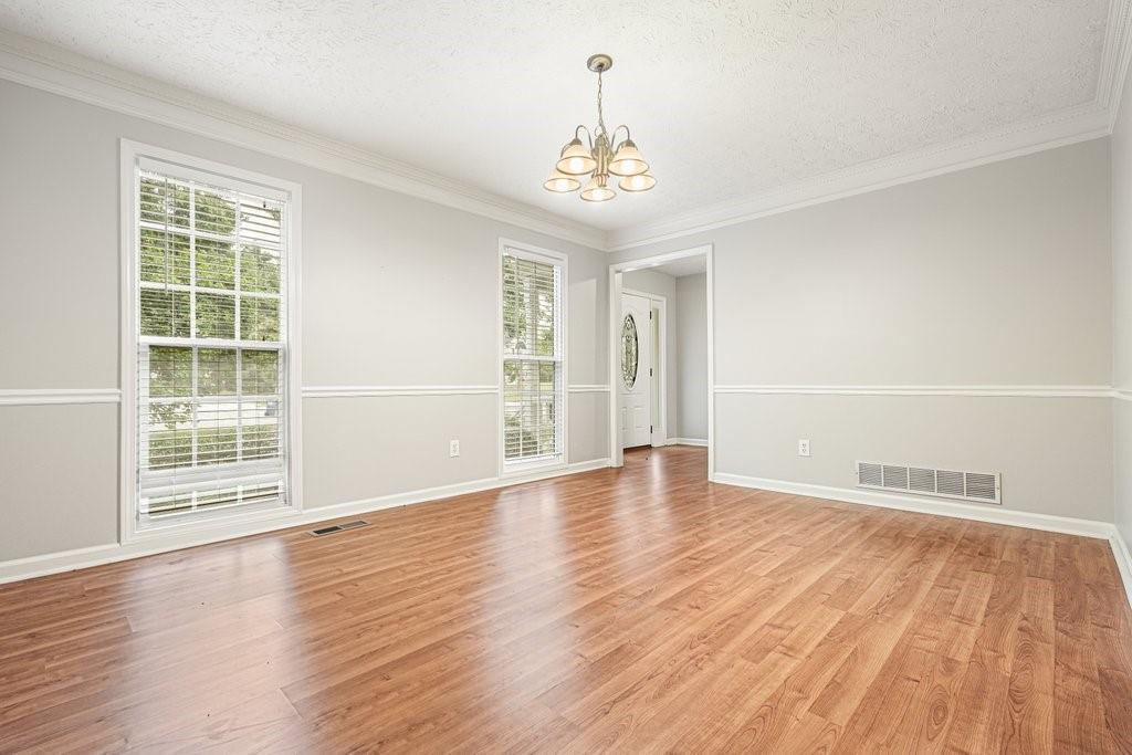 Empty dining room with wood floors, two windows, and a chandelier.