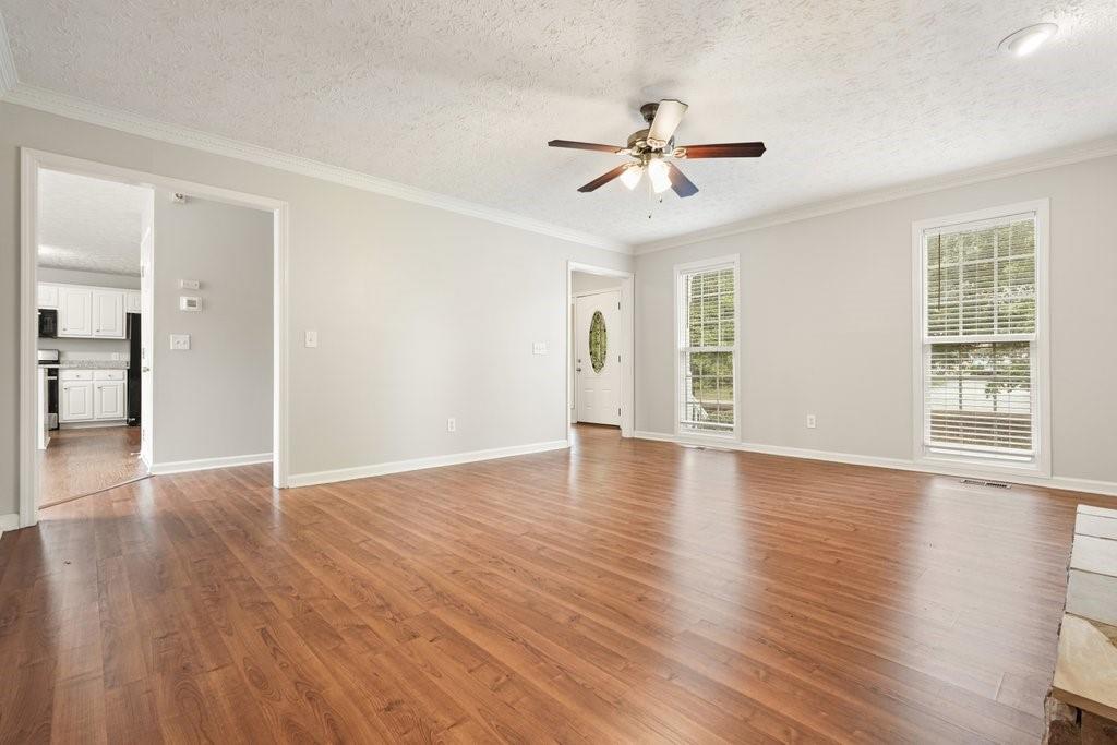 Empty living room with hardwood floors, ceiling fan, and tall windows with blinds.