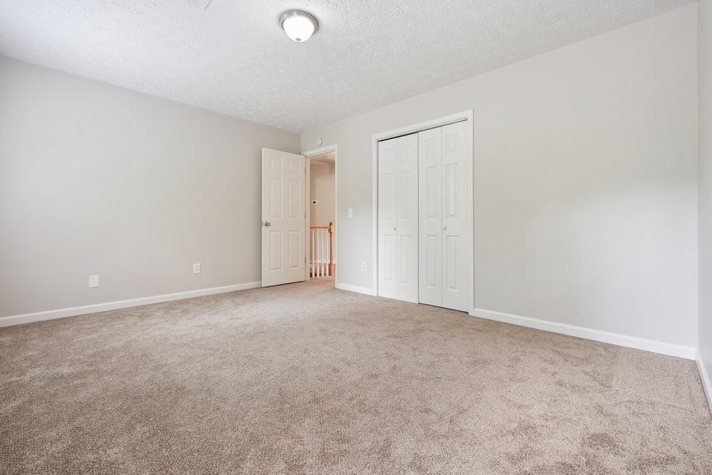 Empty bedroom with beige carpet, a white double-door closet, and an open hallway door.