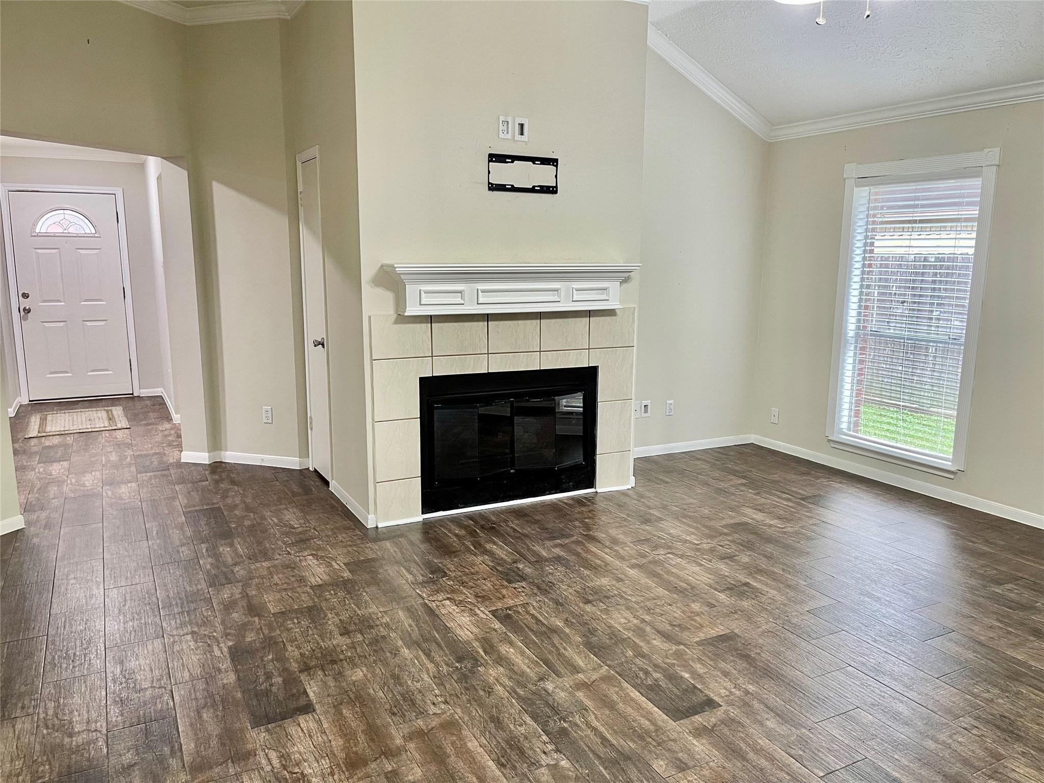 Living room with a tiled fireplace, wood-look floors, and a window beside the entryway.