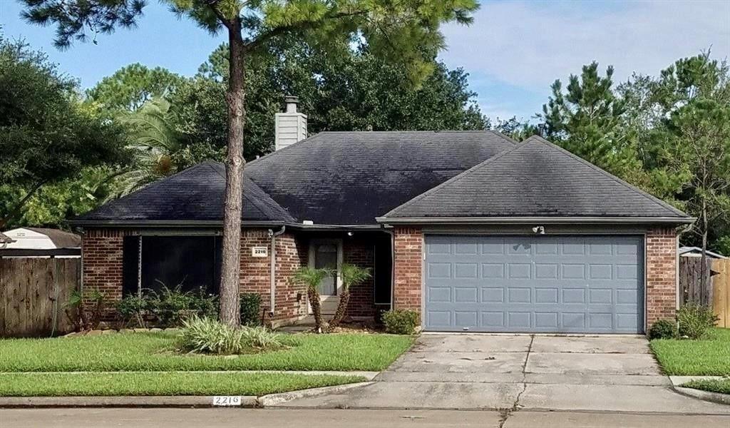 Brick single-story home with a two-car garage and mature trees framing the front.