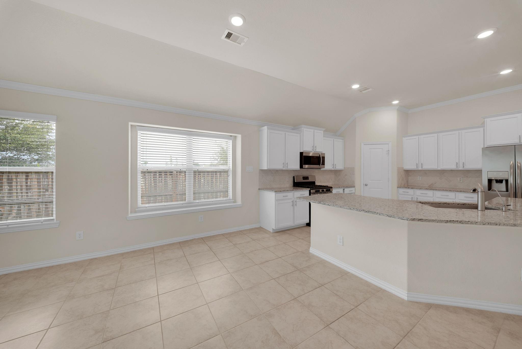 Kitchen with white cabinets, granite island, stainless appliances, and tiled floors.
