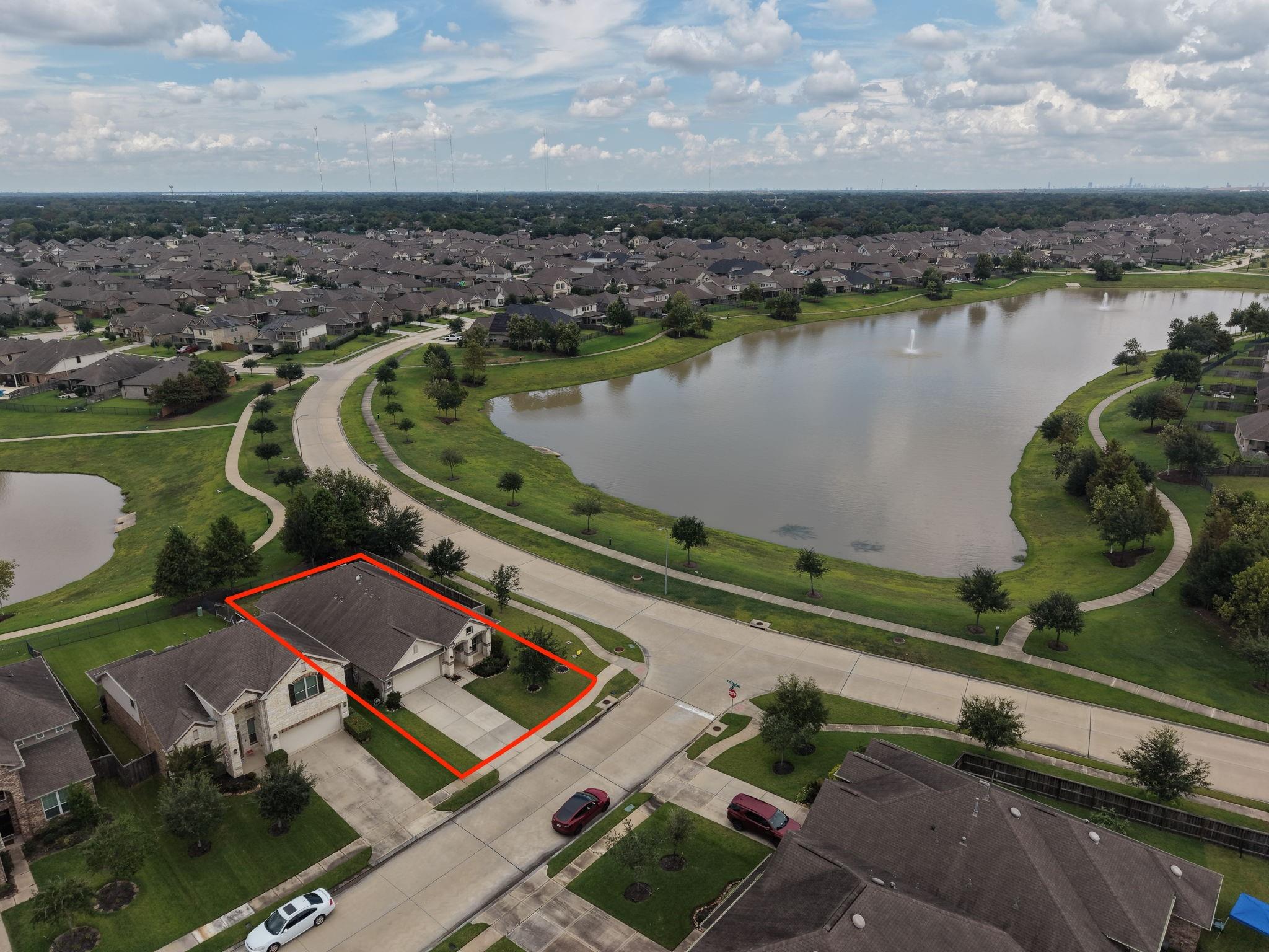 Aerial view of the outlined home beside a neighborhood lake and curving walking paths.