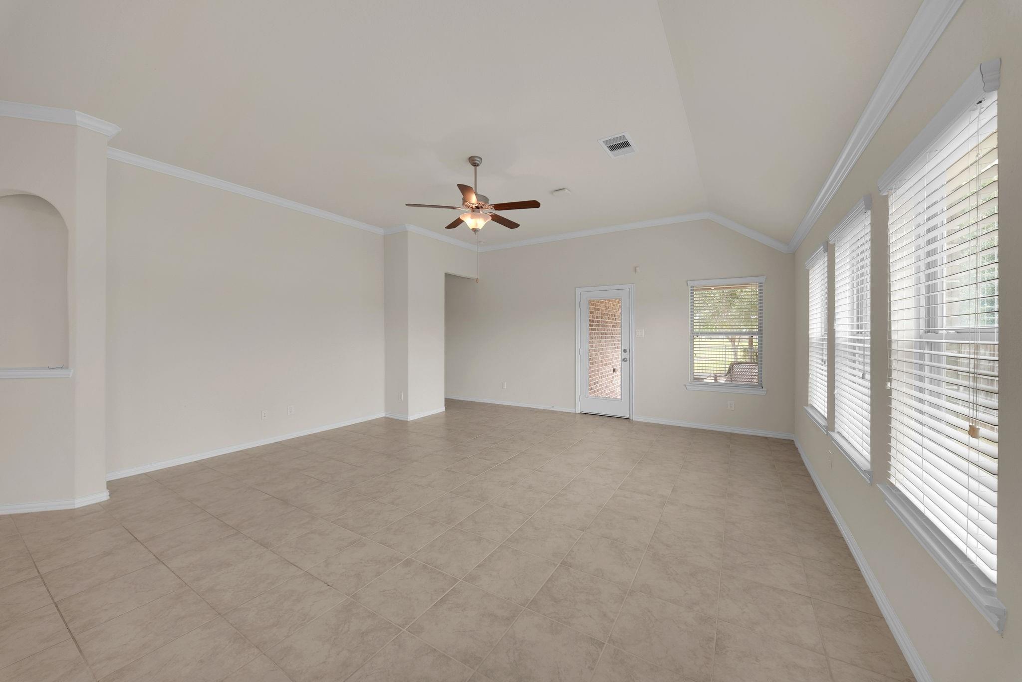 Empty living room with tiled floors, a ceiling fan, and large windows with blinds.