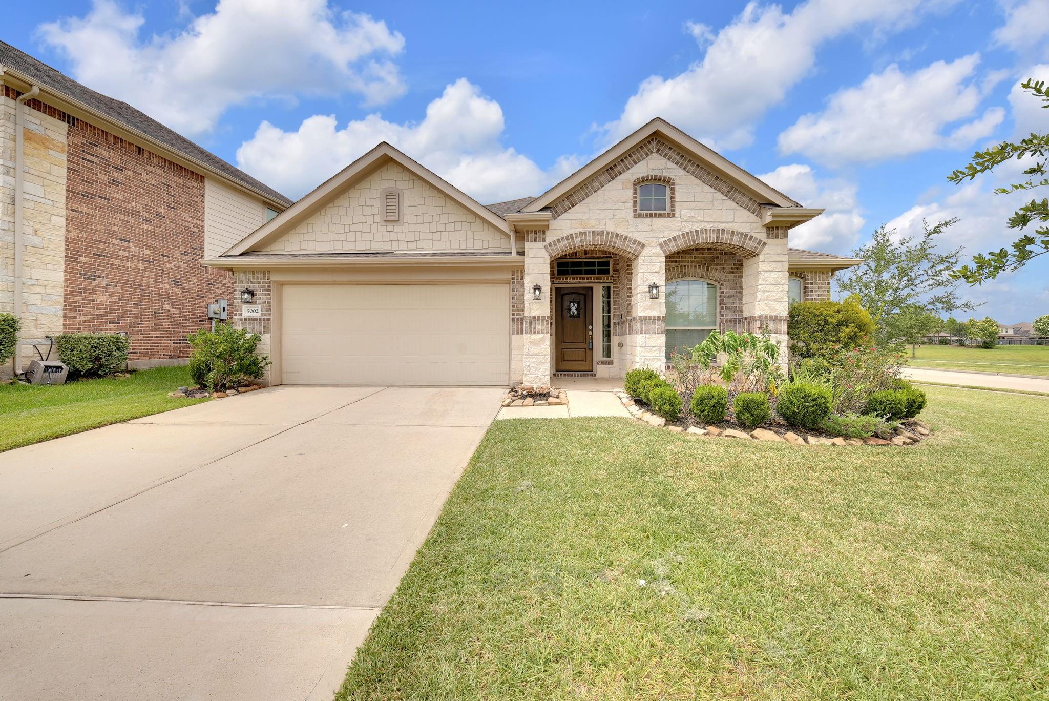 Stone-and-brick home with a two-car garage, arched entry, and landscaped front lawn.