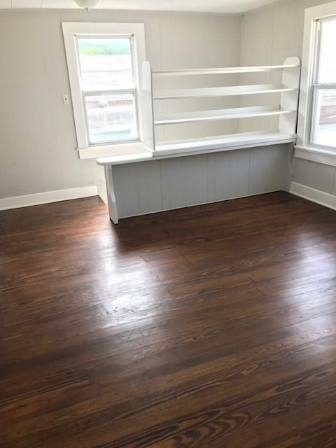 Vacant room with dark hardwood floors, built-in shelving and counter, and two windows.