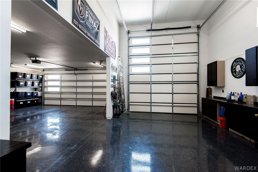 Spacious garage with multiple overhead doors, storage cabinets, and a glossy dark floor.