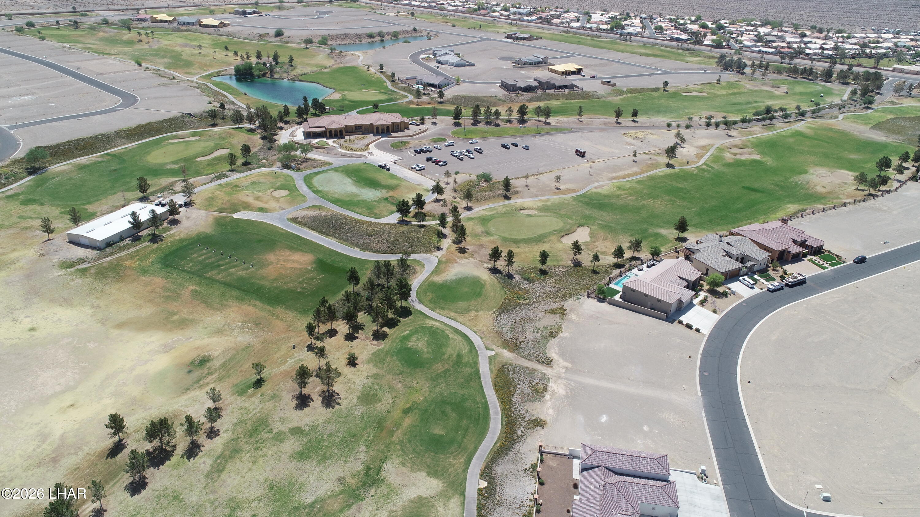 Aerial view of a golf course community with a pond, clubhouse, homes, and winding paths.