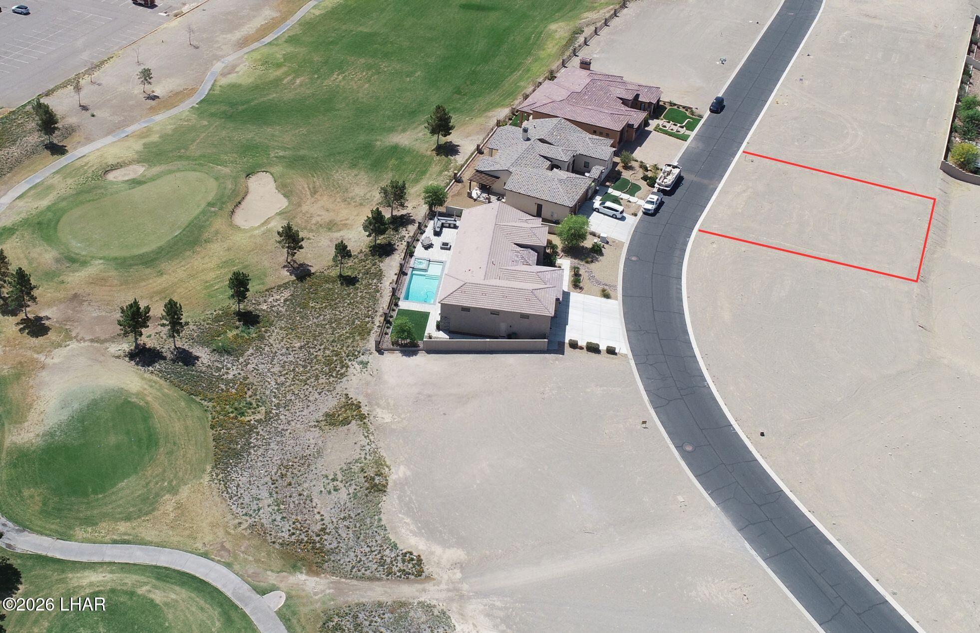 Vacant lot outlined in red beside a curved street, with nearby homes and golf course grounds.