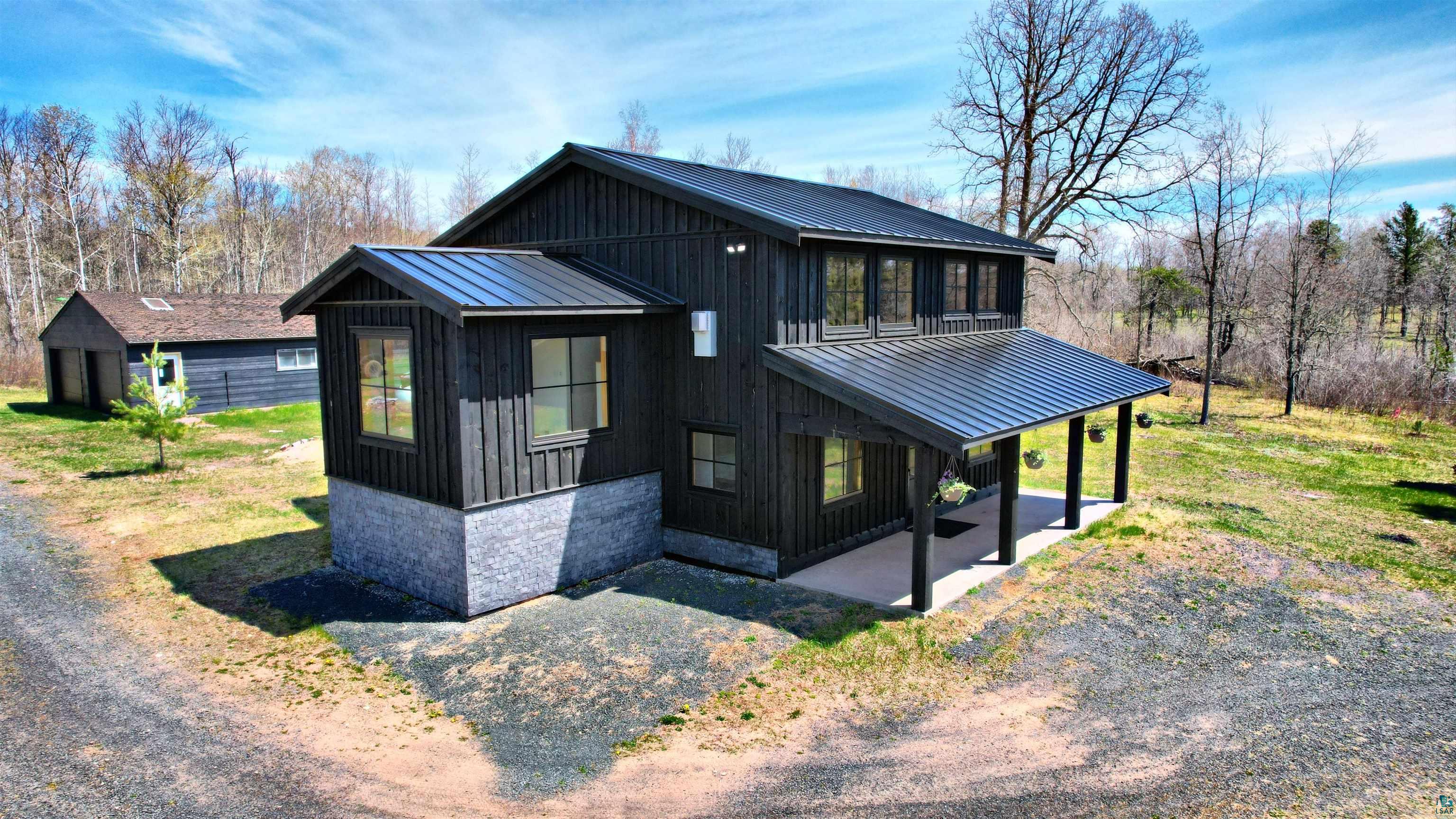 Modern black-sided home with a stone base, metal roofs, and a covered patio.