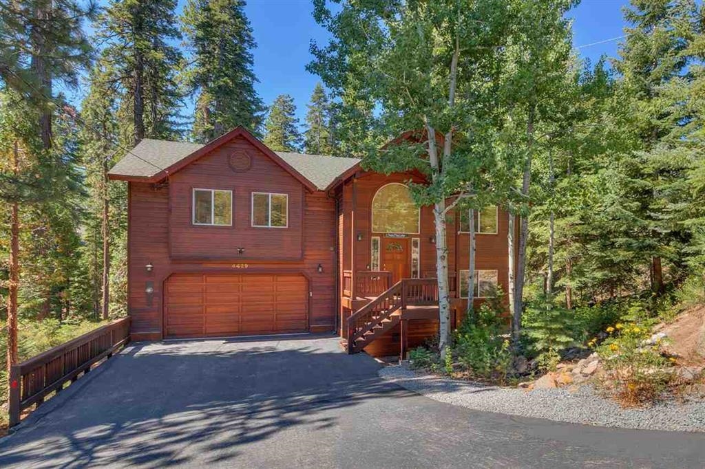 Wood-sided house with a double garage and raised porch, surrounded by pine trees.