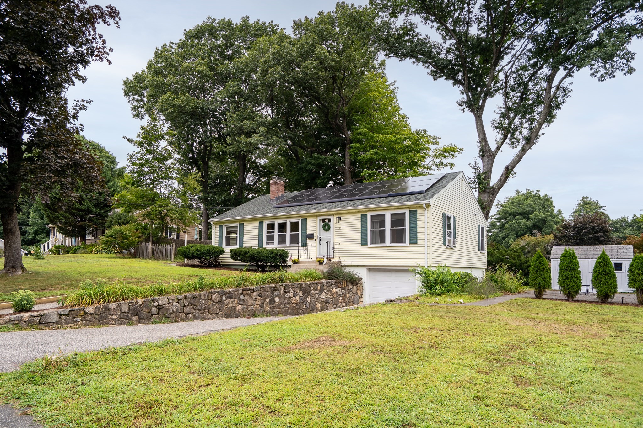 Cream split-level home with rooftop solar panels, a stone retaining wall, and a sloped lawn.