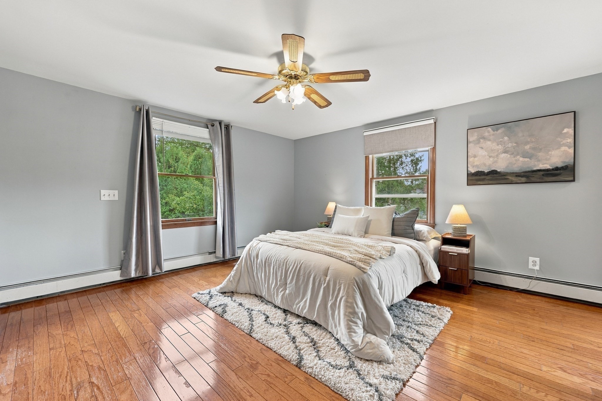 Bedroom with a white bed, warm hardwood floors, two windows, and a ceiling fan.