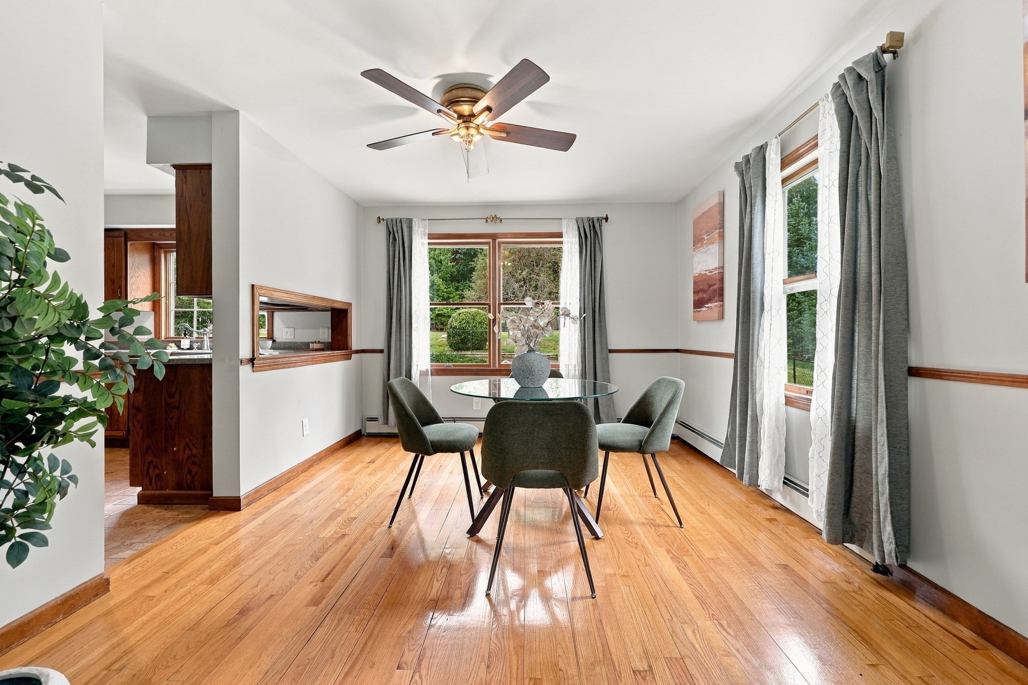 Dining room with a glass table, four chairs, hardwood floors, and large curtained windows.