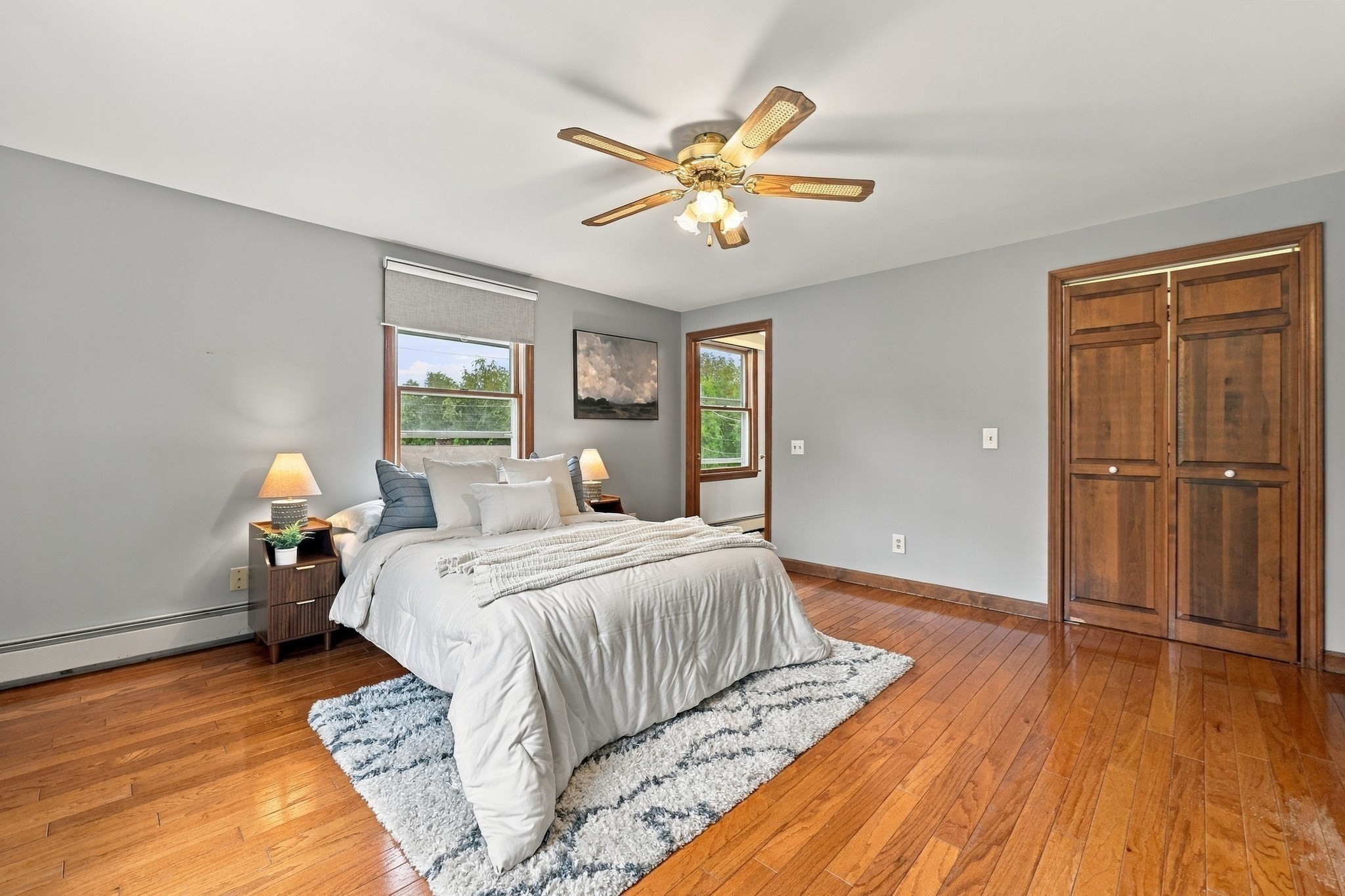 Furnished bedroom with a white bed, polished hardwood floors, and wood double closet doors.