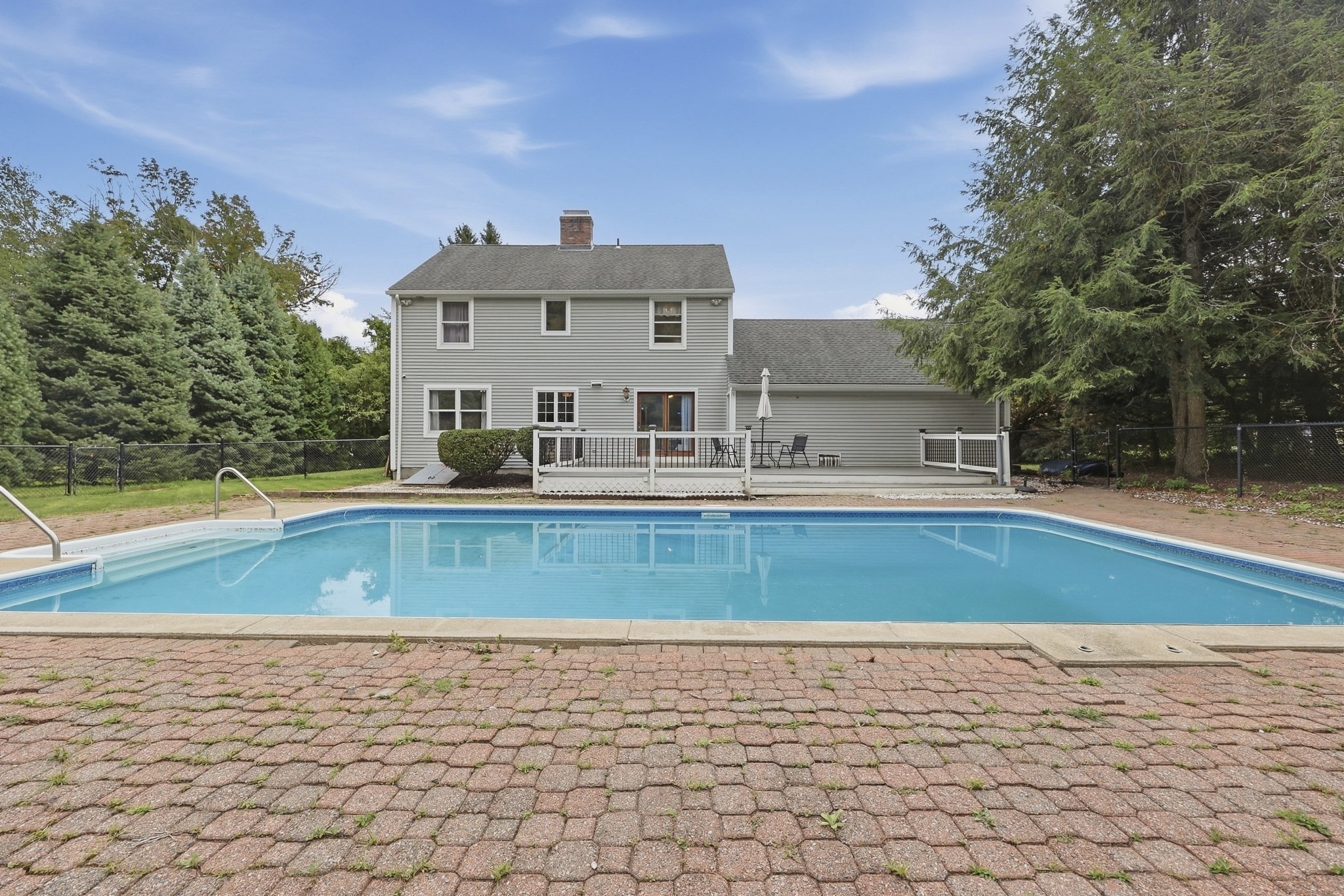 Rear of a gray two-story house beyond a large in-ground pool and brick patio.