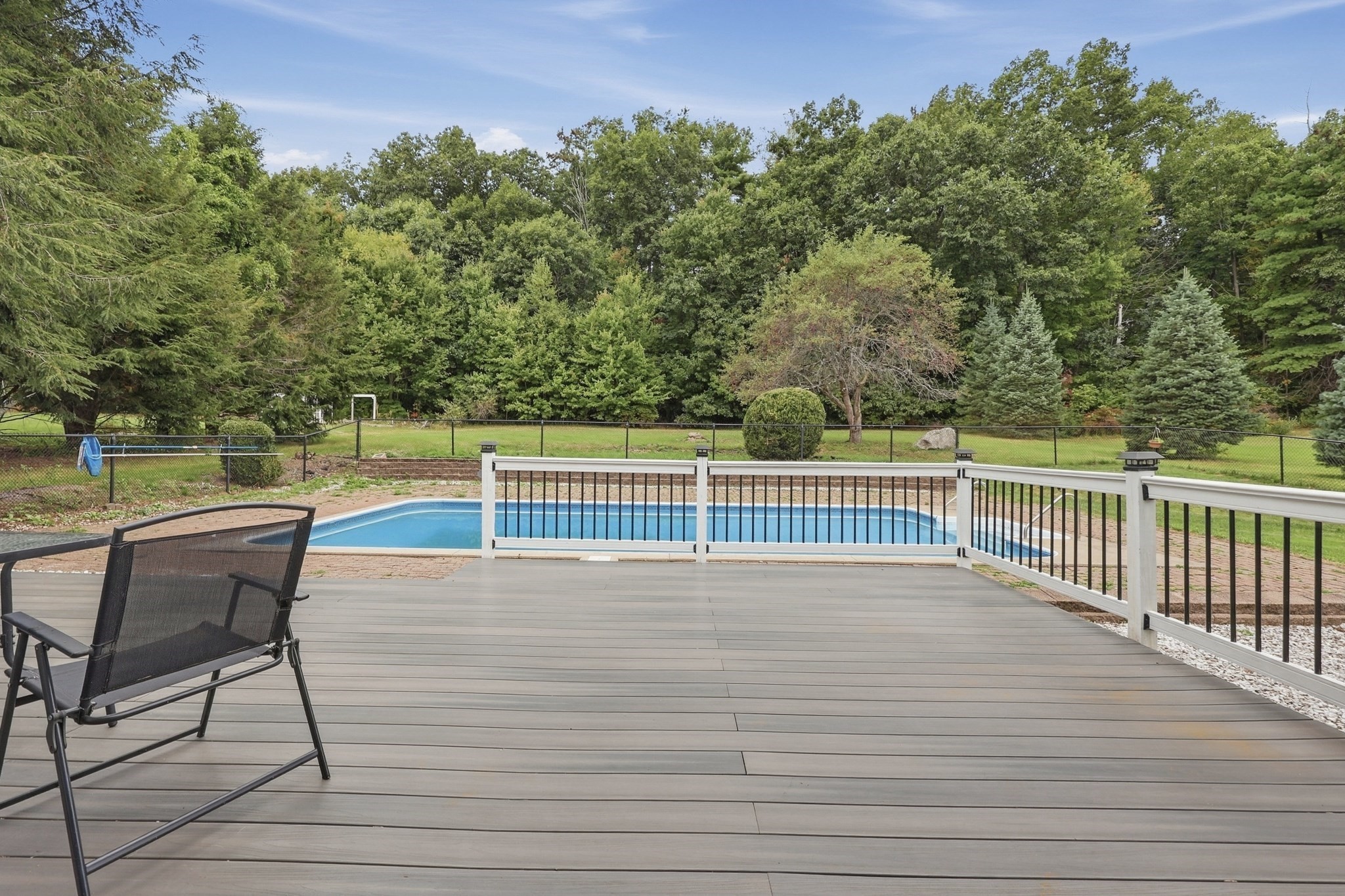 Composite deck and patio chair overlooking a fenced swimming pool and tree-lined yard.