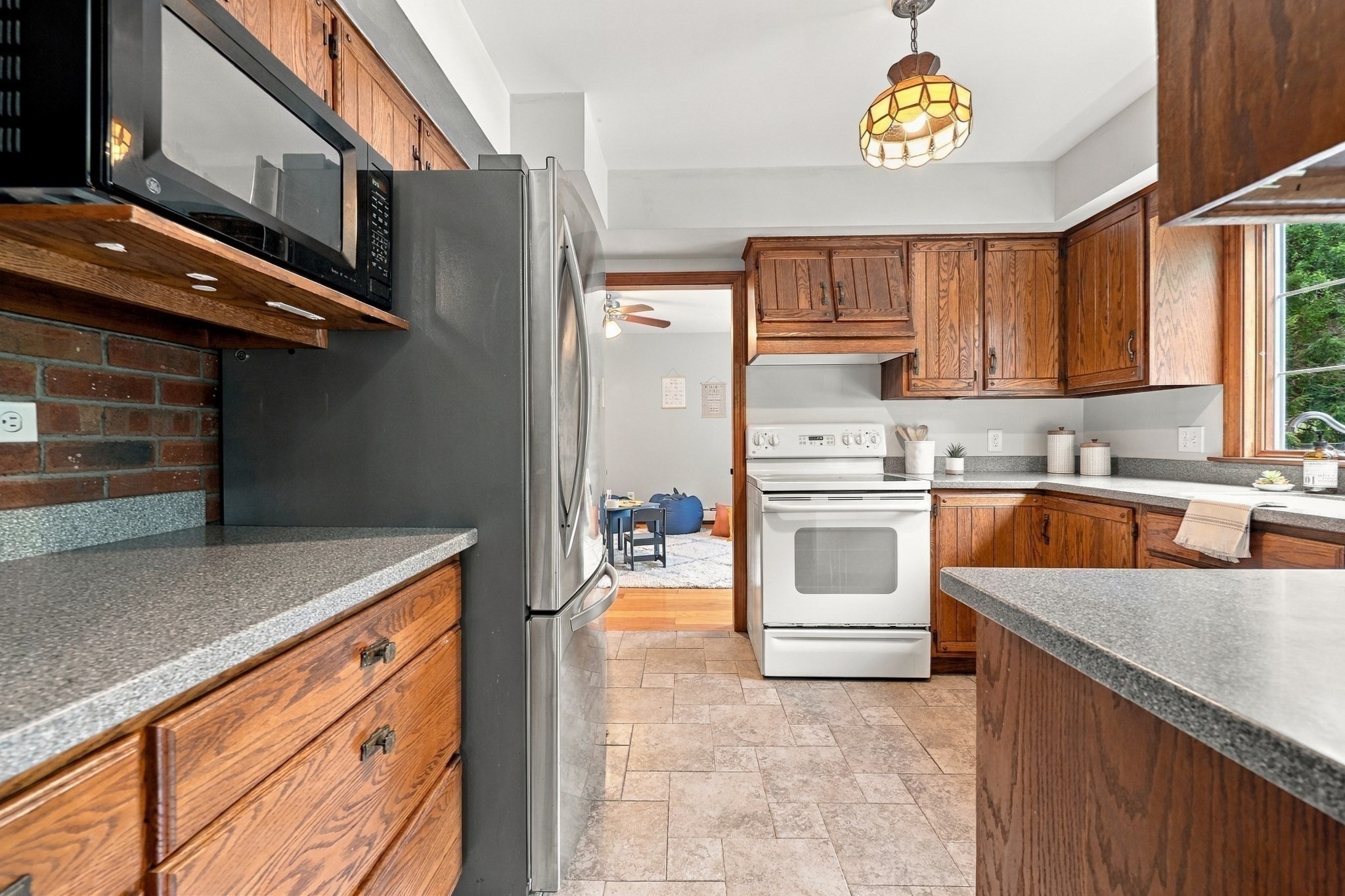 Kitchen with warm wood cabinets, brick backsplash, stainless-steel refrigerator, and a stained-glass pendant light.