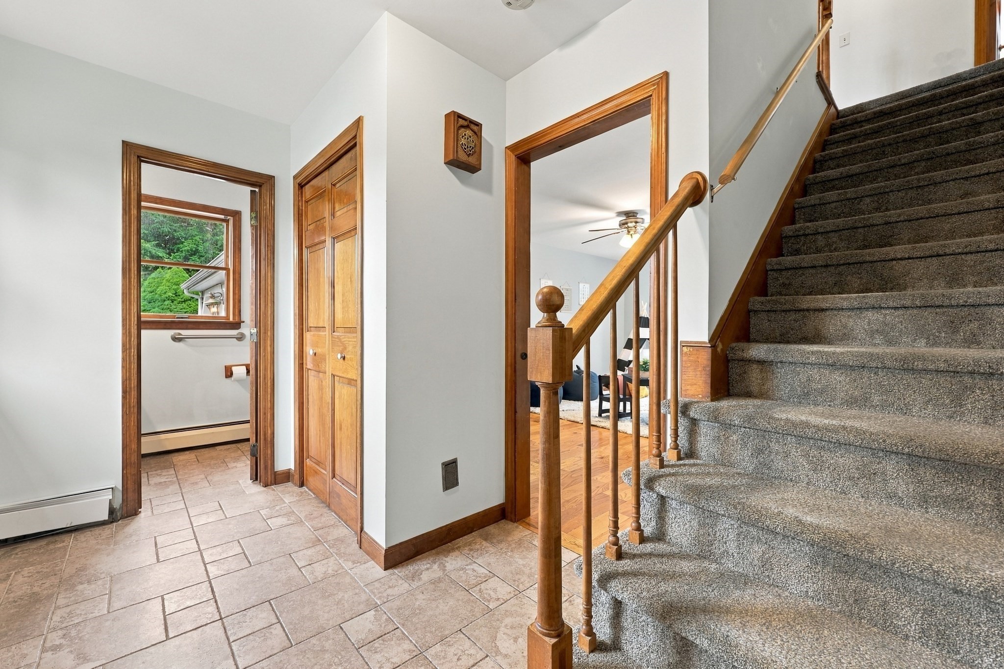 Home entryway with tiled floor, wooden trim, carpeted stairs, and doorways to a bathroom and living room.