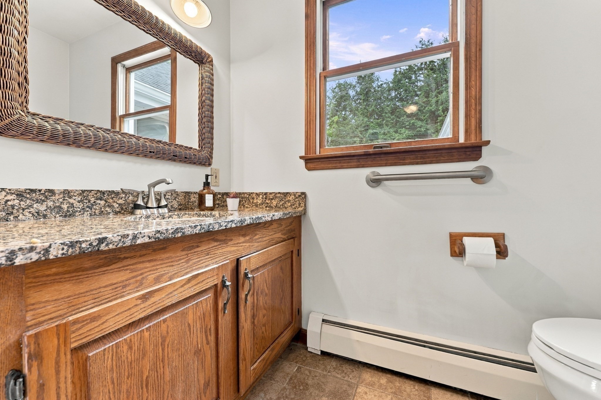 Bathroom with a wood vanity, granite countertop, and wood-trimmed window overlooking trees.