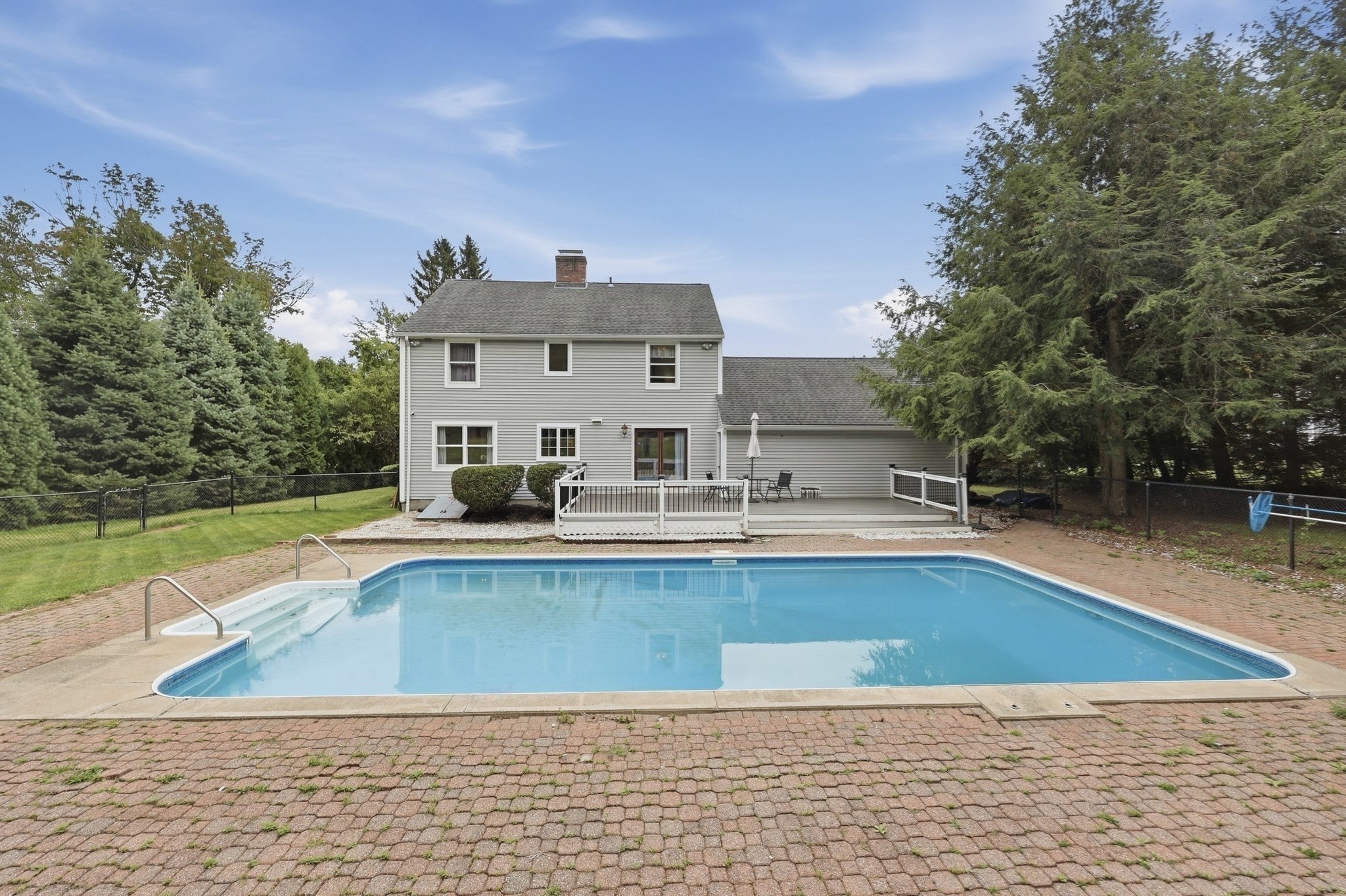 Rear of a gray two-story house behind a large in-ground pool, with a deck and fenced yard.