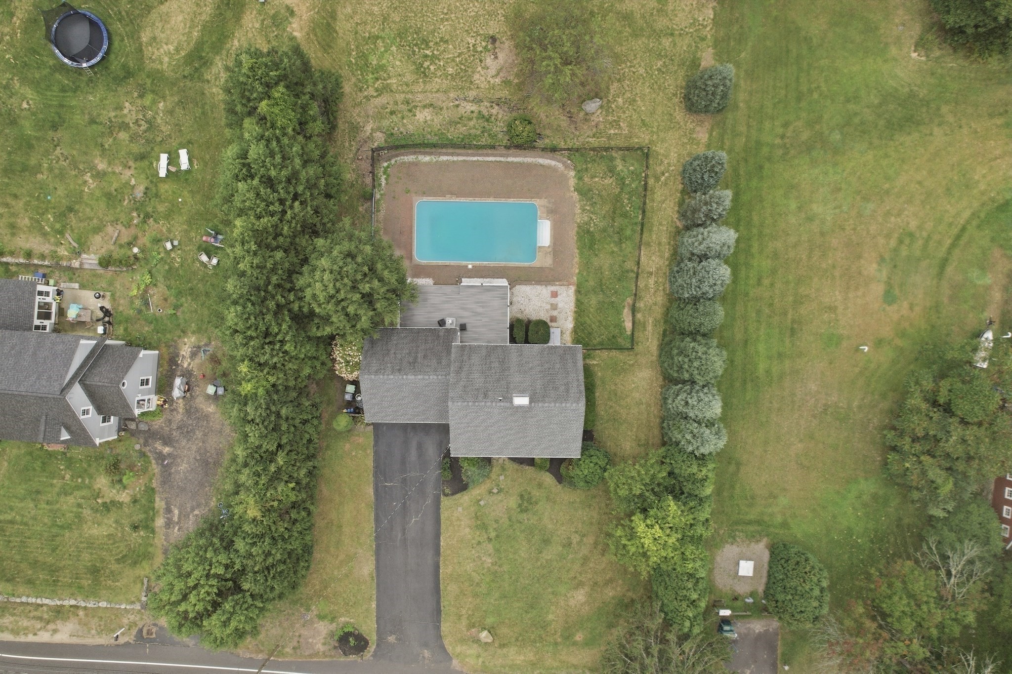 Aerial view of a house with a backyard pool, long driveway, and mature trees.