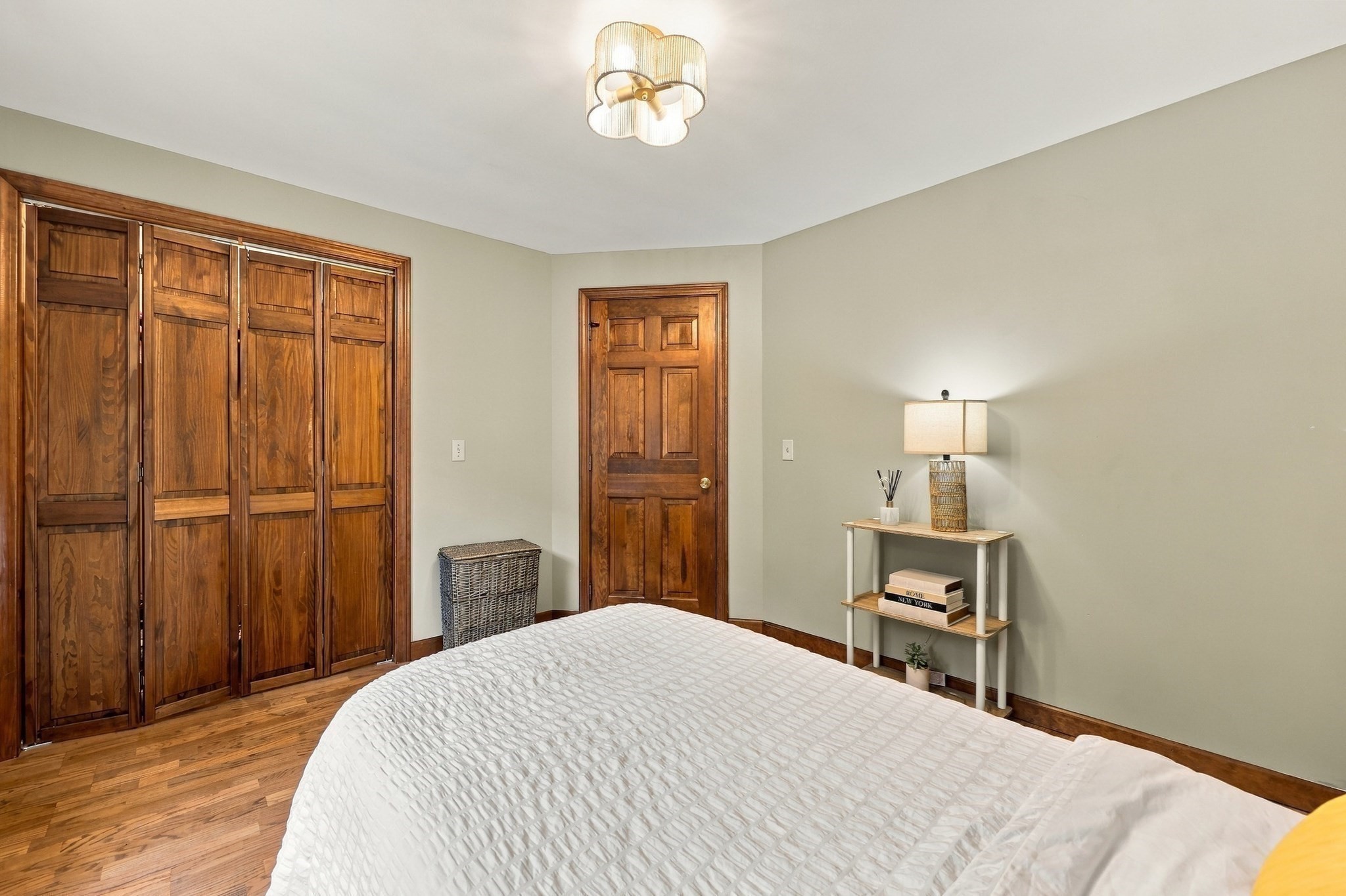 Bedroom with a white bed, hardwood floors, and distinctive wood closet doors.