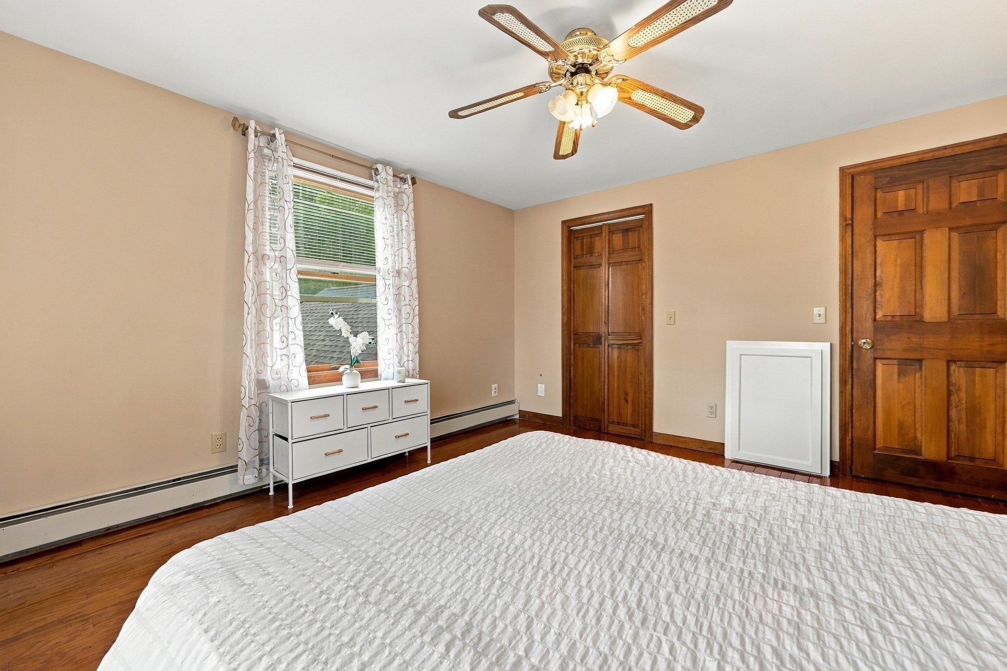 Bedroom with a white quilted bed, hardwood floors, and warm wood doors.