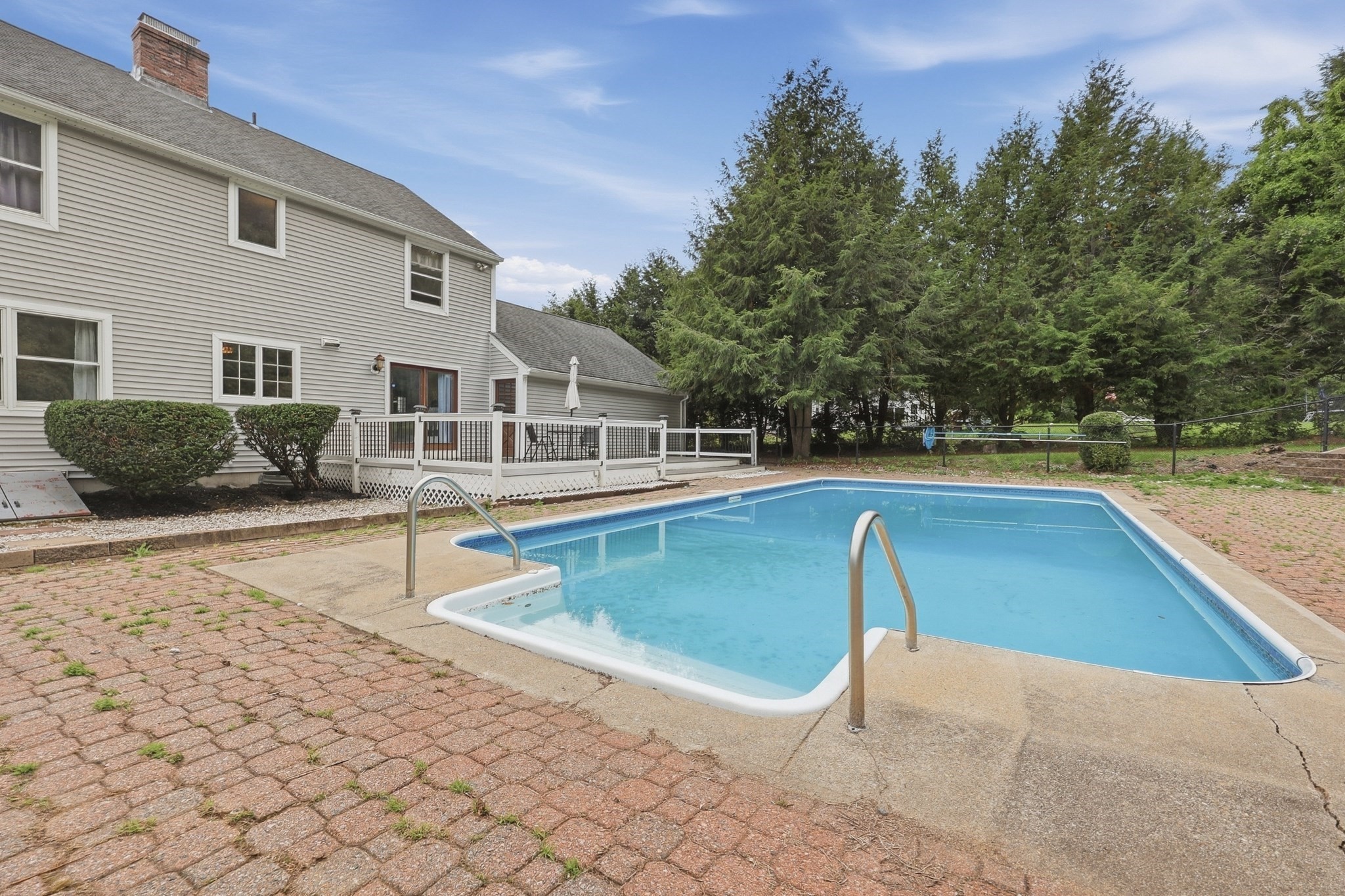 Backyard swimming pool beside the home’s deck and gray-sided exterior.