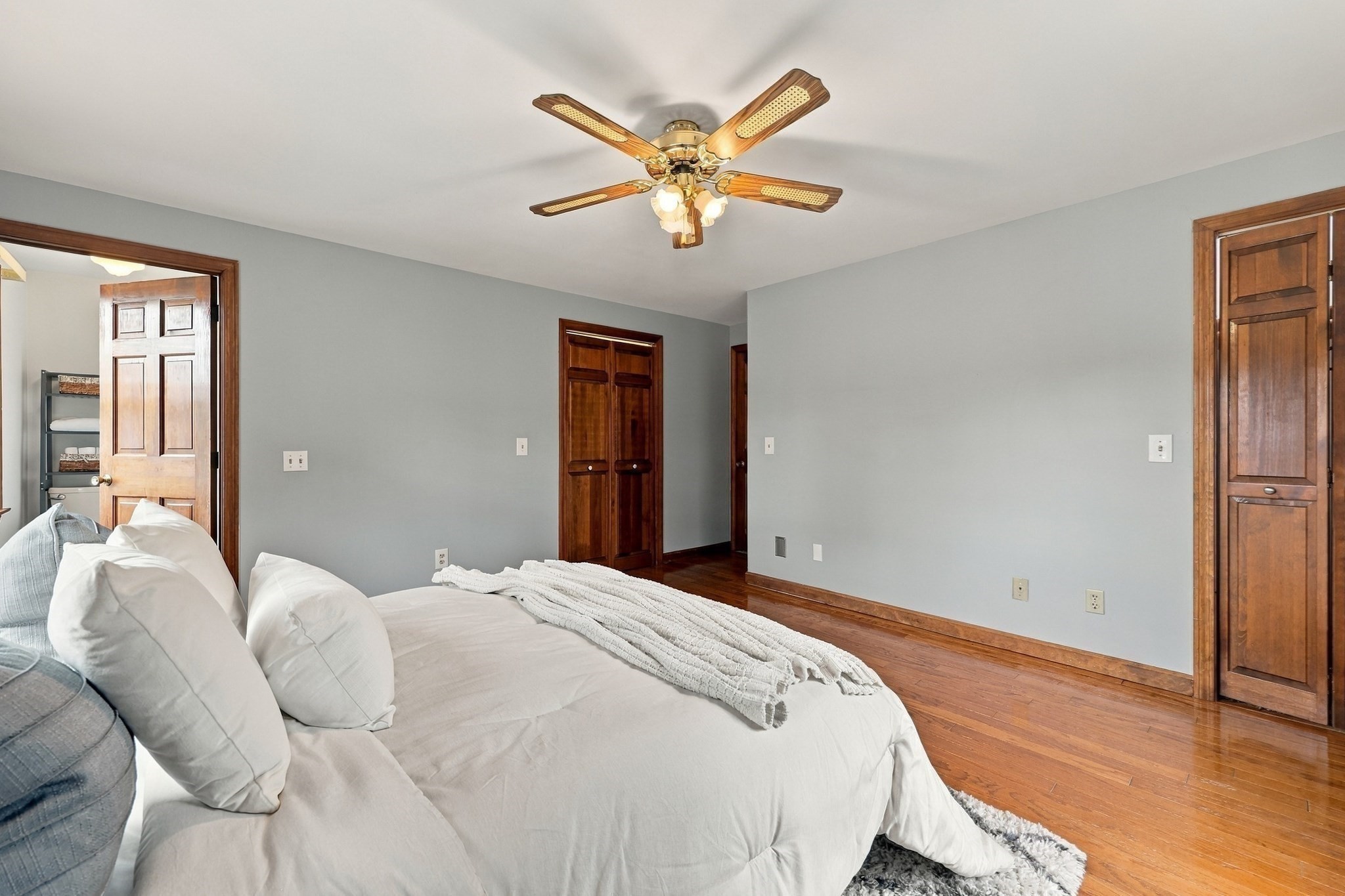 Bedroom with white bedding, hardwood floors, and a wood-blade ceiling fan.