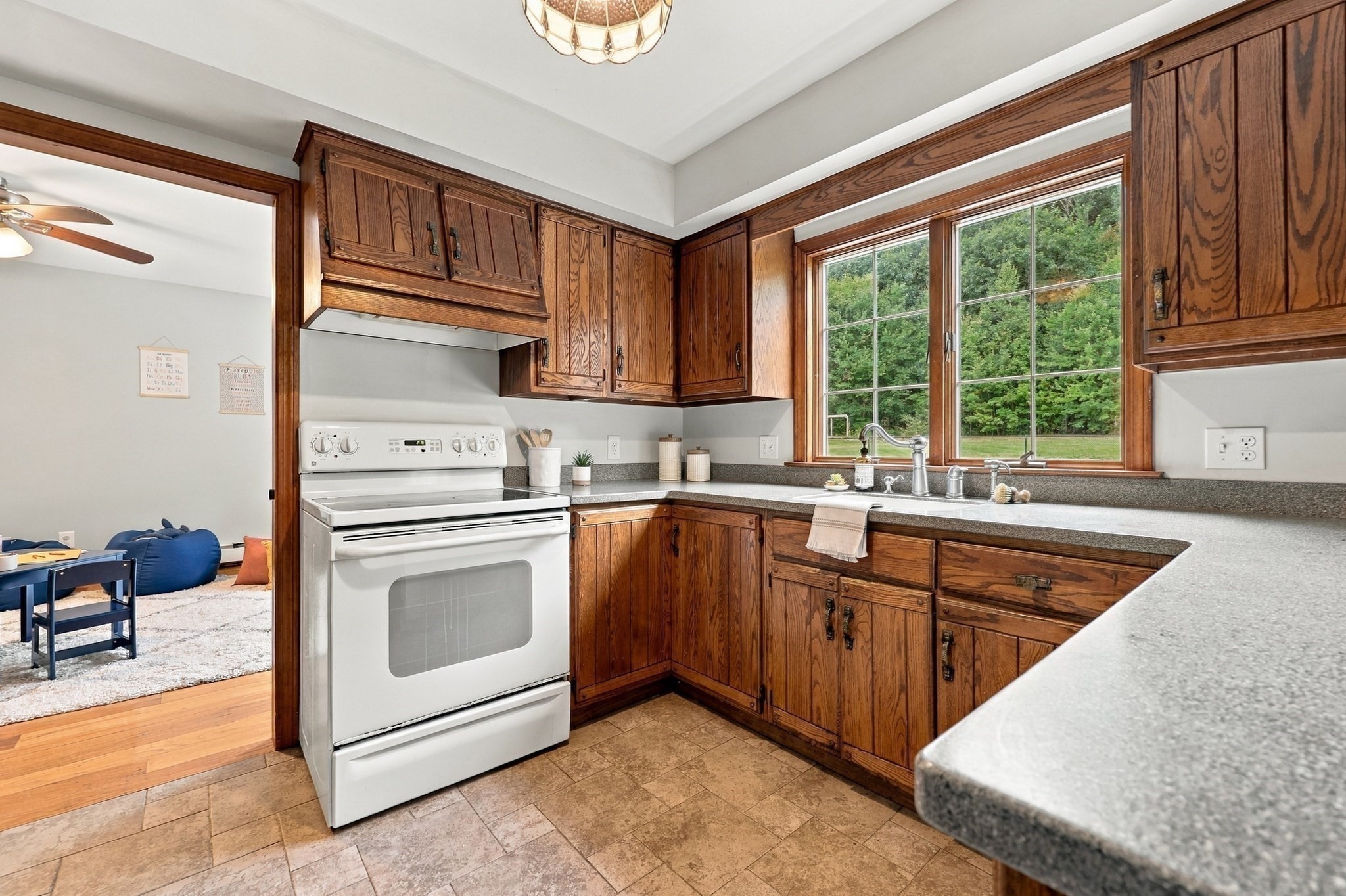 Kitchen with warm wood cabinets, a large tree-facing window, and a white electric range.