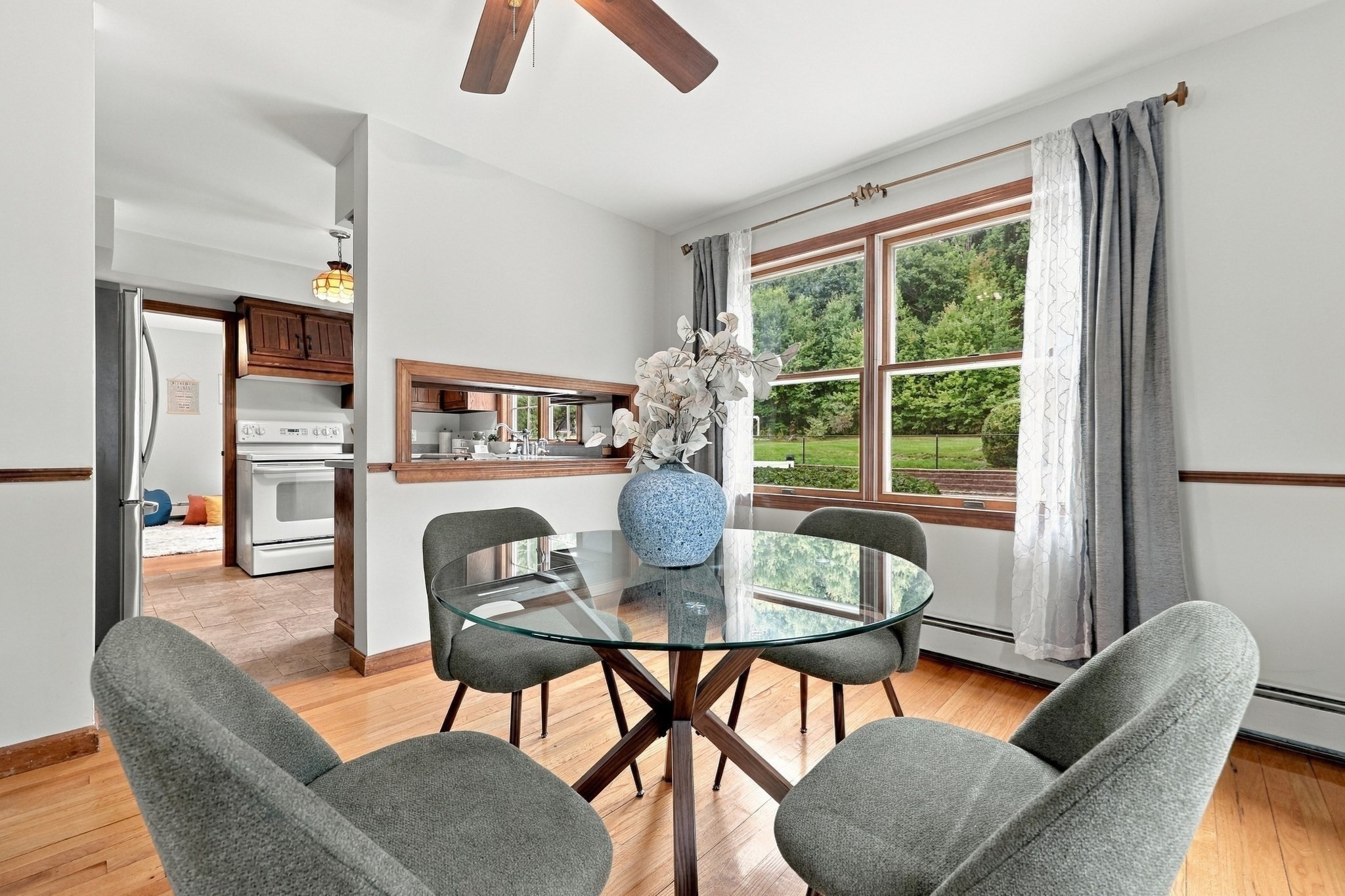 Dining area with a glass table, gray chairs, and a large window overlooking the yard.