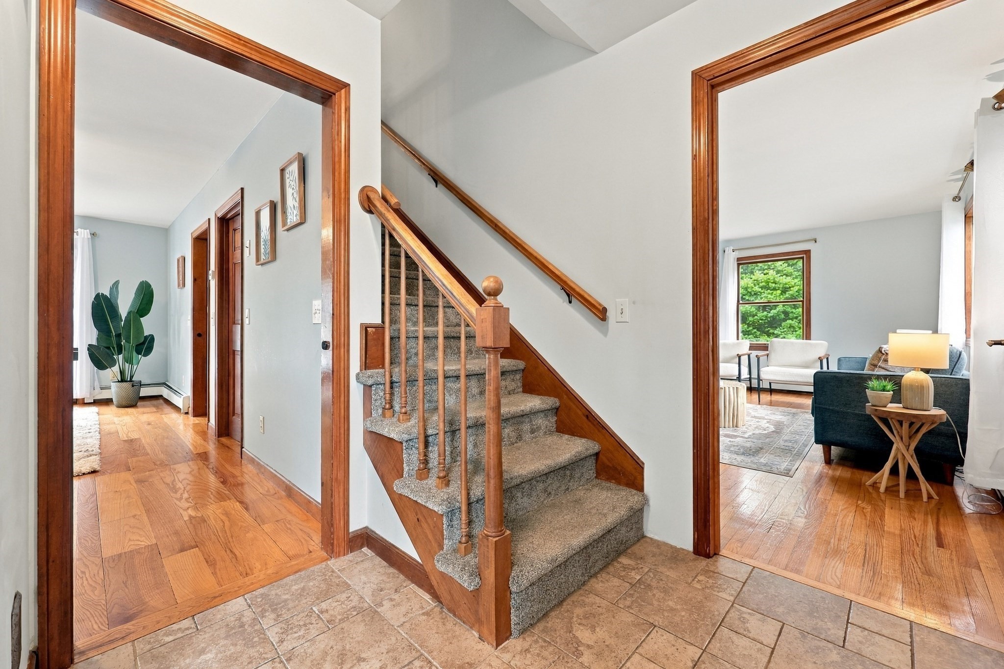 Entryway with carpeted staircase, wood handrail, tiled floor, and a furnished living room beyond.