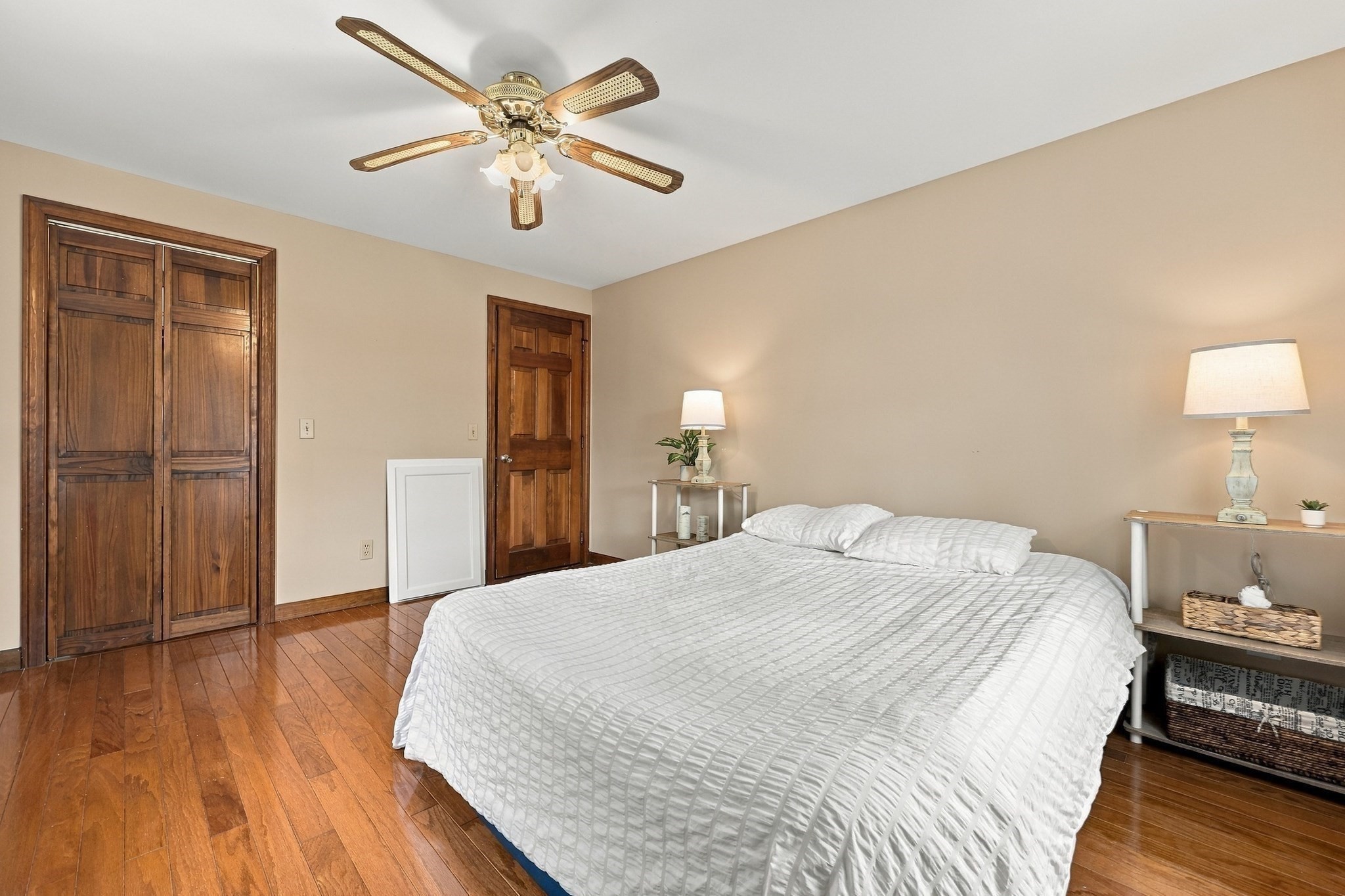Bedroom with a large white bed, polished hardwood floors, and dark wood closet doors.