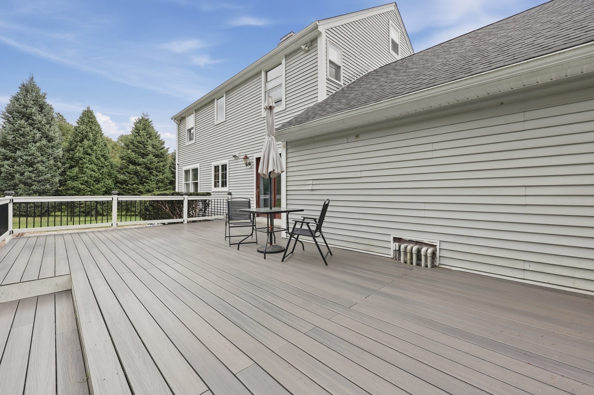 Wide gray deck beside a light-gray house, furnished with black patio chairs and a table.