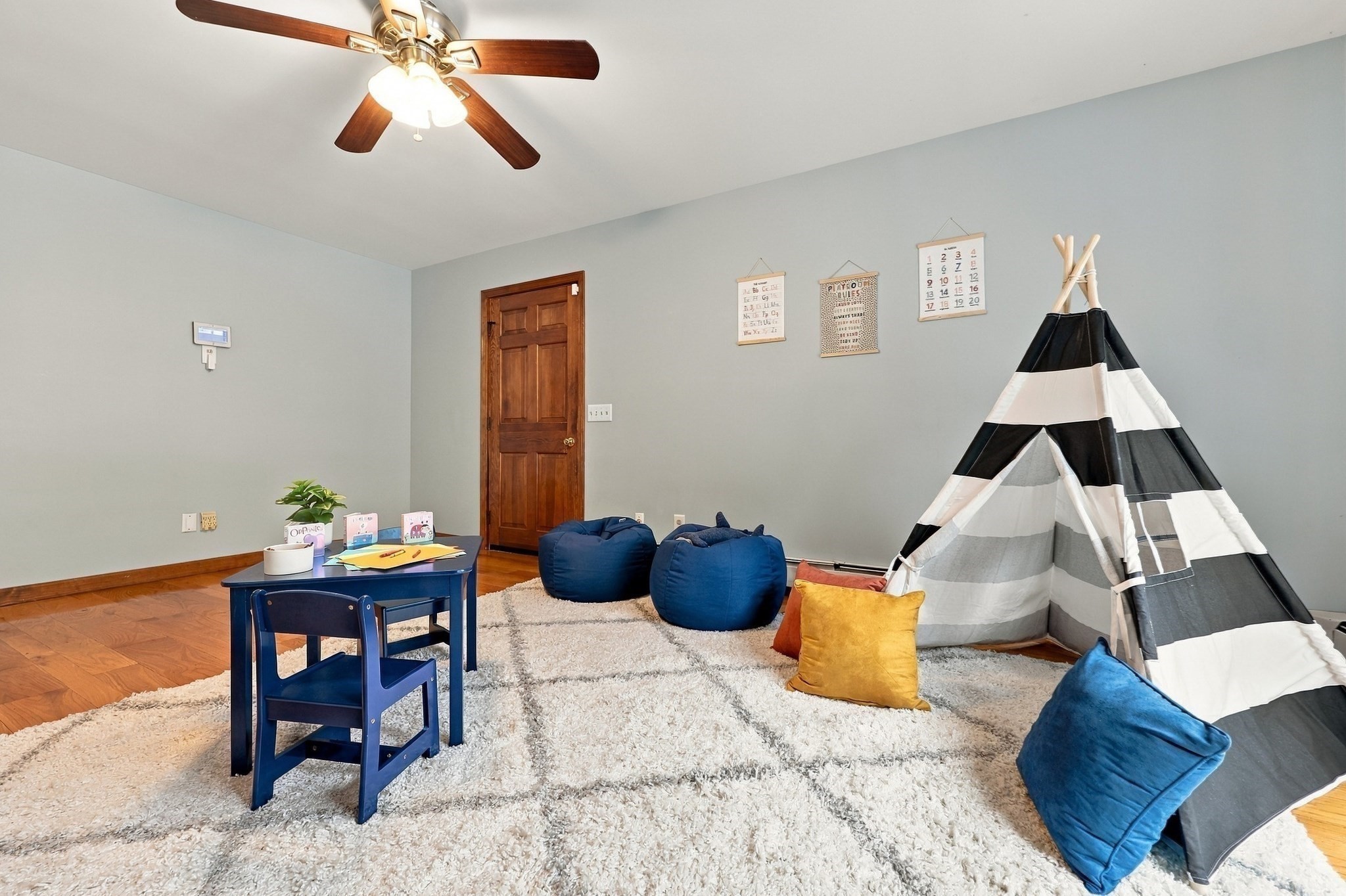 Furnished playroom with a striped teepee, blue beanbag chairs, and a small table on a shag rug.