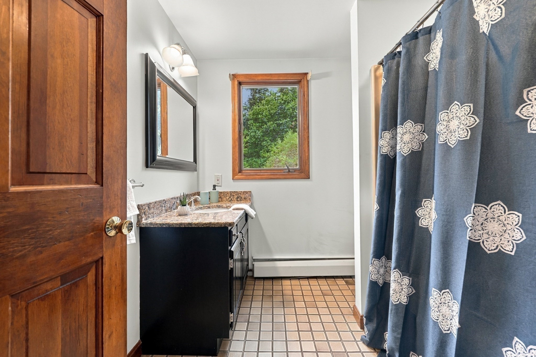 Bathroom with dark vanity, tiled floor, wood-trimmed window, and blue patterned shower curtain.